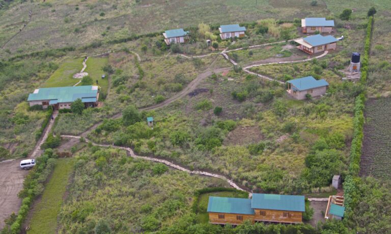 Alt-Text: Vogelperspektive auf afrikanische Lodges mit grünen Dächern inmitten der Landschaft.
