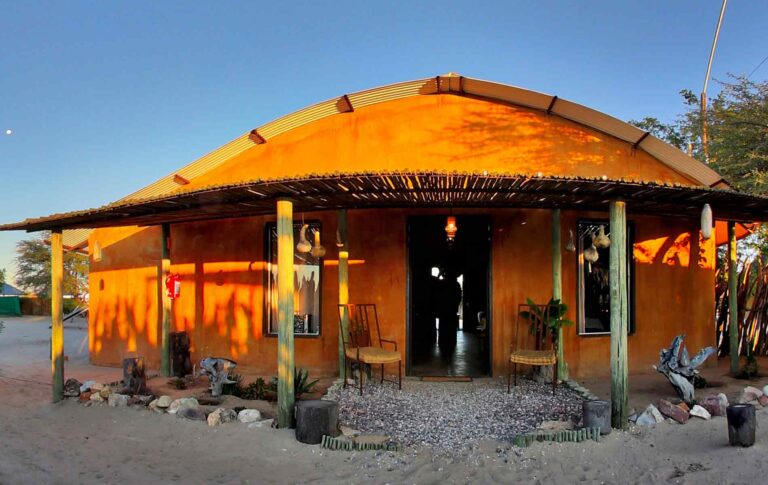 Gemütliche afrikanische Lodge mit Sandboden, Holzstühlen und natürlicher Dekoration.