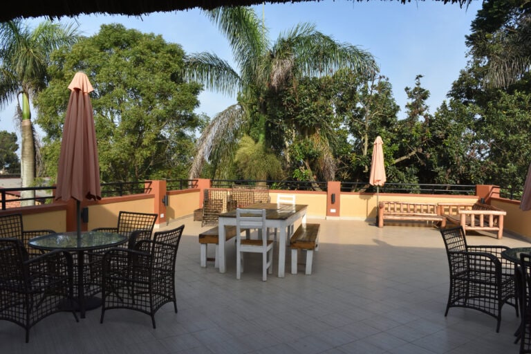 Heller, einladender Balkon mit Tischen und Stühlen, umgeben von tropischen Bäumen, ideal für Afrika-Reisetraum.