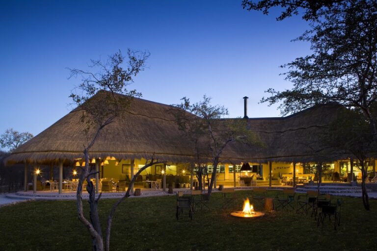 Ergänzte Sonnenuntergangsszene in einer afrikanischen Safari-Lodge mit Lagerfeuer und gemütlicher Atmosphäre.