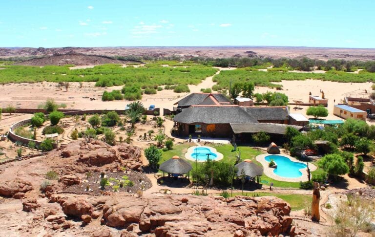 Luxus Safari-Lodge mit Pool in der afrikanischen Wildnis, umgeben von Wüstenterrain und grünen Oasen.