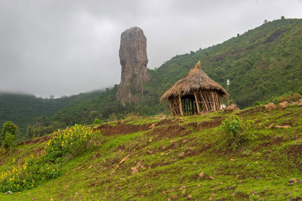 Traditionelles afrikanisches Haus auf grüner Hügellandschaft mit Felsen.