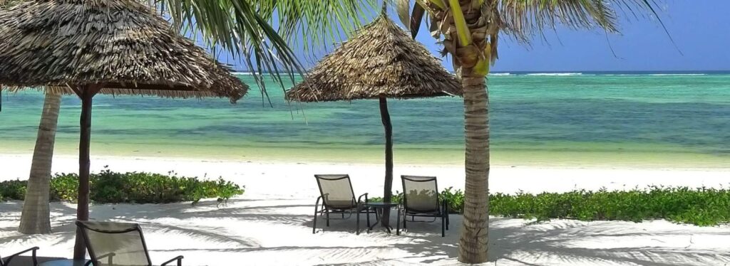 Sonnenliegen unter Palmen am weißen Strand mit Blick auf das türkisblaue Meer, ideal für Afrika-Urlaub.