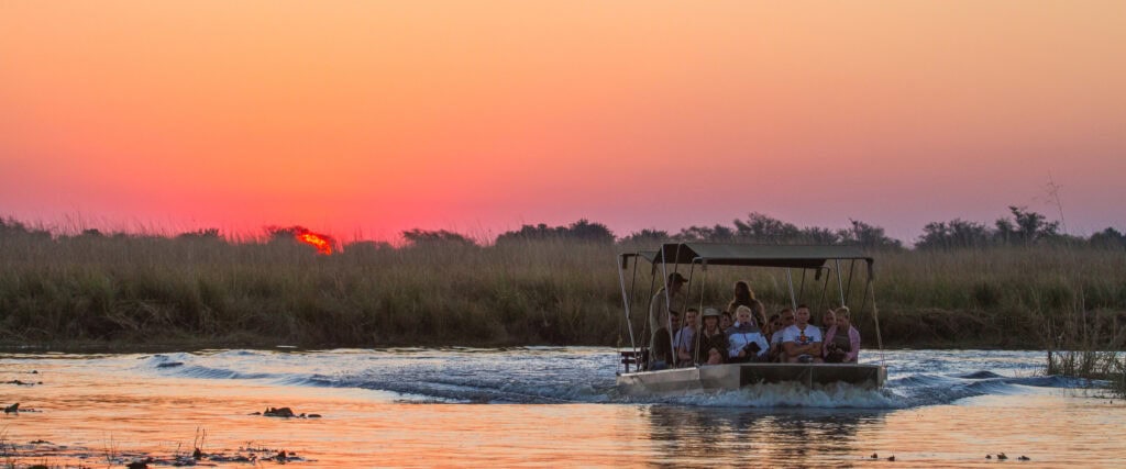 Boot auf Fluss mit Safari-Touristen während Sonnenuntergang in Afrika, Tierbeobachtung, Naturlandschaft.