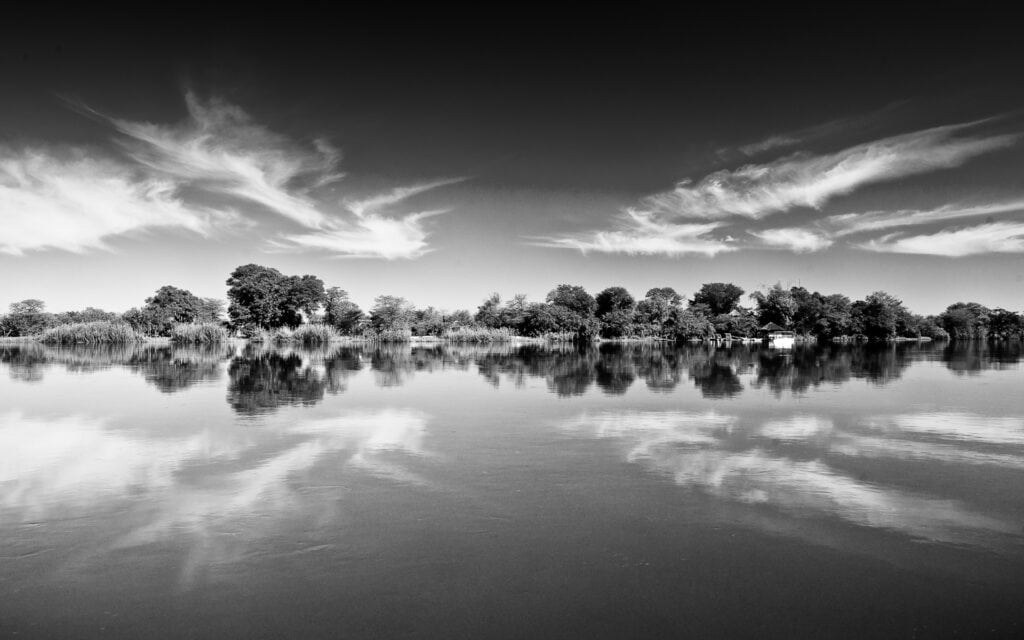 Schwarz-Weiß-Bild einer afrikanischen Flusslandschaft mit Bäumen und Wolken, ideal für Safari- und Naturreisen in Afrika.