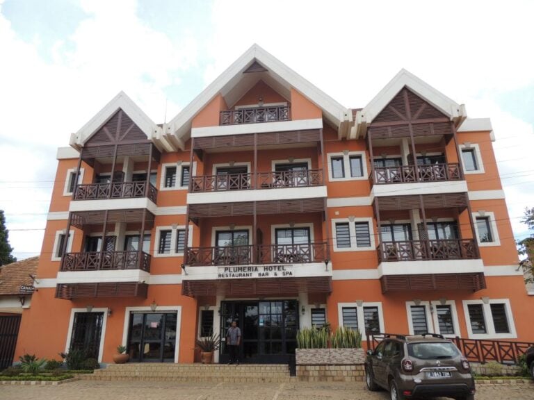 Mehrstöckiges afrikanisches Hotel mit traditionellen Holzveranden, blühender Umgebung und Blick auf die Stadt.