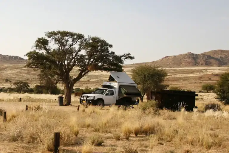 Alt: Safari Wohnmobil in afrikanischer Savanne mit Baum und Bergen im Hintergrund.