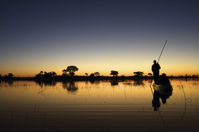 Silhouette von zwei Menschen auf einem Boot auf dem Wasser bei Sonnenuntergang.