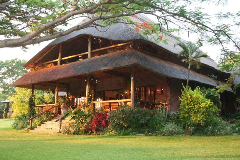 Auffälliges Bild einer afrikanischen Safari-Lodge mit traditioneller Architektur, umgeben von Natur und tropischen Pflanzen.