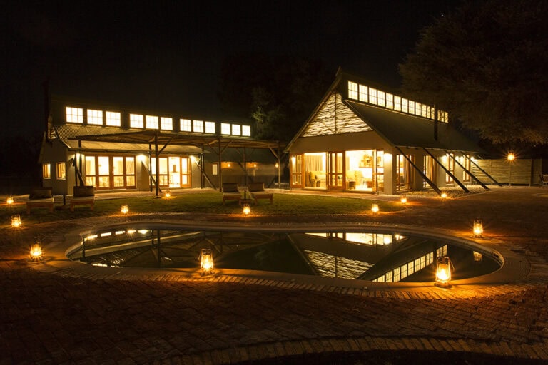 Gemütliche afrikanische Lodge bei Nacht, warm erleuchtete Unterkunft mit Swimmingpool.
