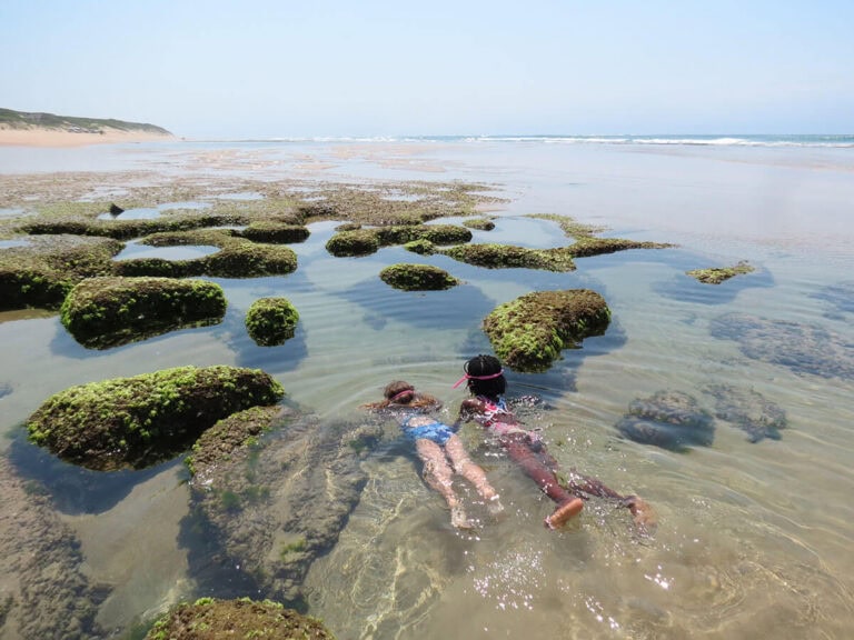 Strand mit Felsen, klarer Ozean, Kinder beim Schnorcheln in Afrika.