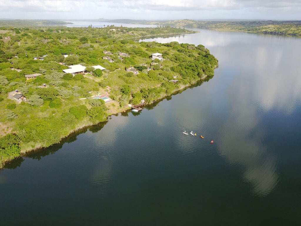 Aerialaufnahme eines afrikanischen Flusses mit grüner Uferlandschaft und Kajakfahrern.