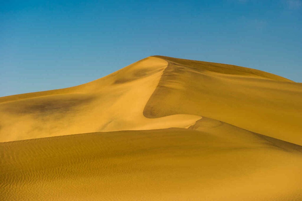 Sanddüne in der afrikanischen Wüste unter blauem Himmel.