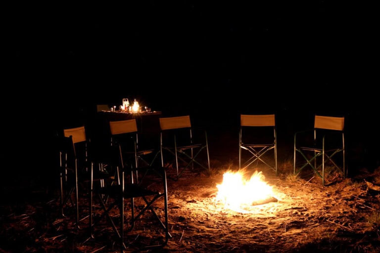Alt: Afrikanisches Lagerfeuer bei Nacht mit Campingstühlen und Kerzen, afrikanische Safari Erfahrung.