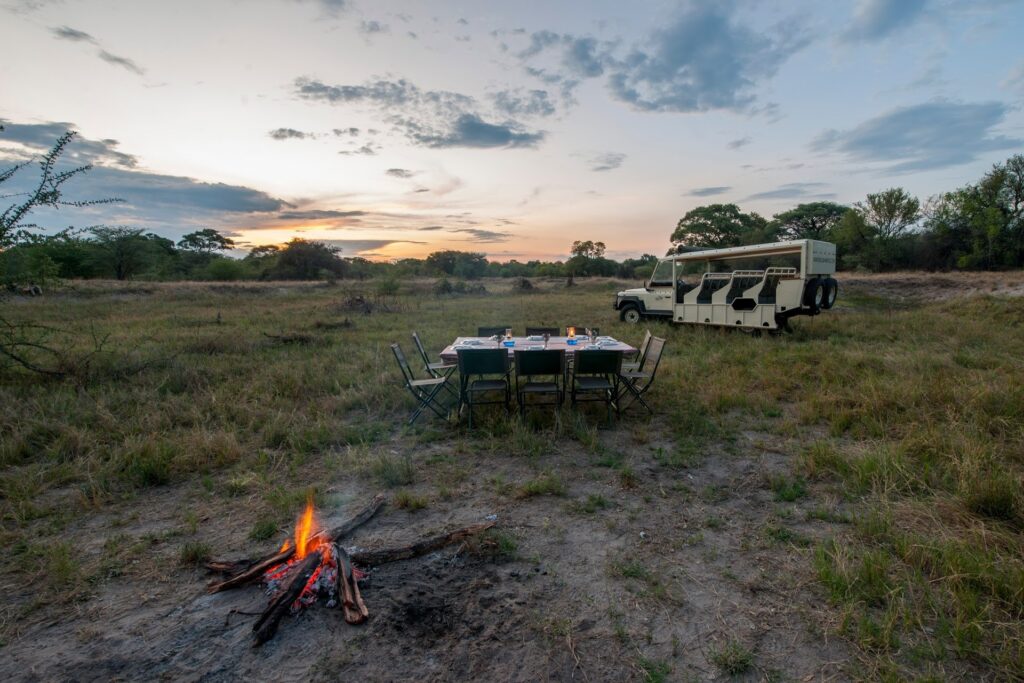 Alt-Text: Camping im Busch in Afrika mit Lagerfeuer, Safariwagen und Dinner im Freien.