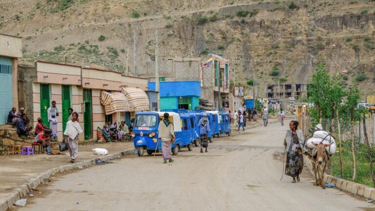 Buntes Dorf in Afrika mit Straßenverkehr, Einheimischen und Berghintergrund, perfekte Afrika-Reise.