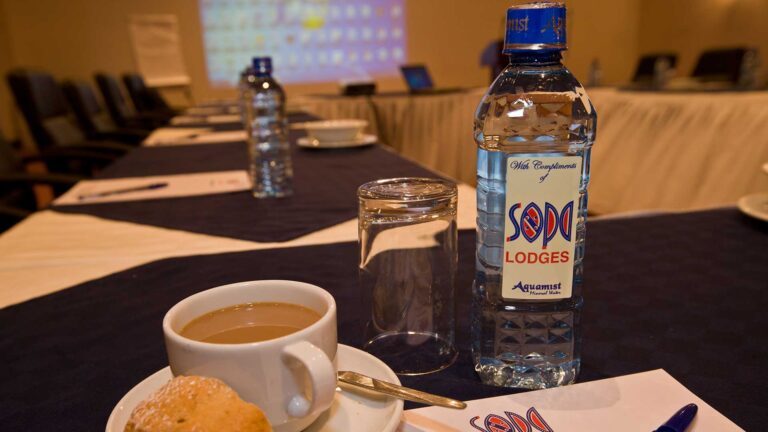 Alt Text: Wasserflasche mit einem Glas auf einem gedeckten Tisch in einer afrikanischen Lodge.