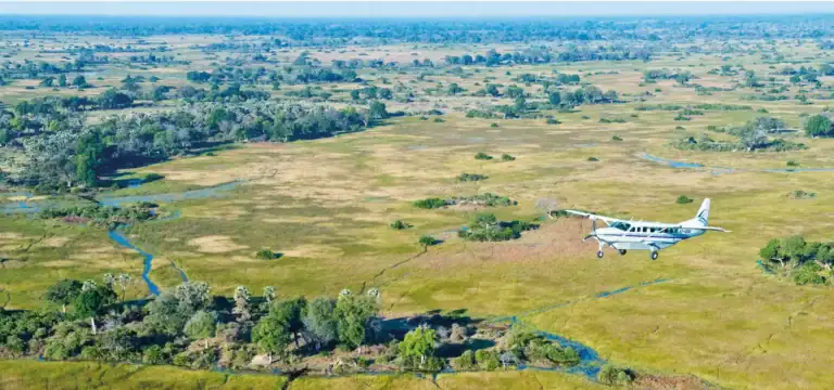 Hubschrauber fliegt über die weiten, grünen Savannen Afrikas mit Flüssen und Wildtieren.