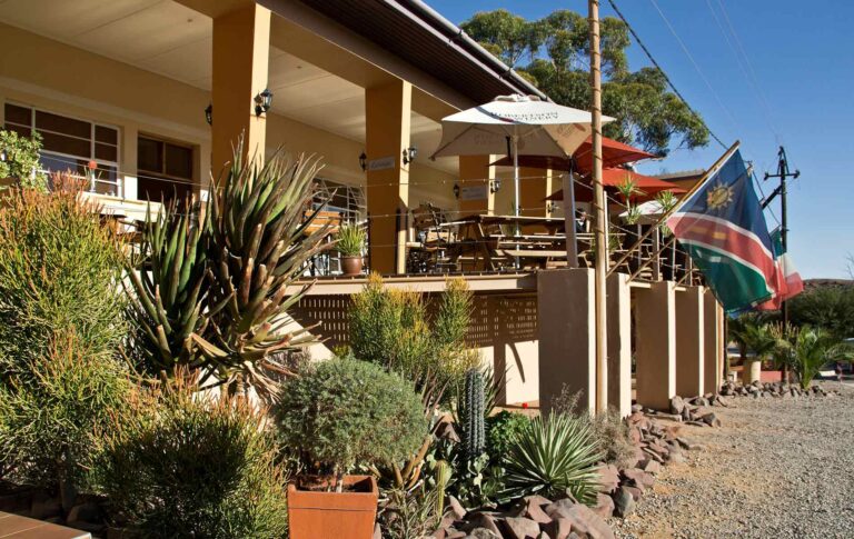 Gemütliche Terrasse eines Cafés in Namibia mit südafrikanischen Flagge, Kakteen und Wüstenpflanzen, typische afrikanische Reiseatmosphäre.