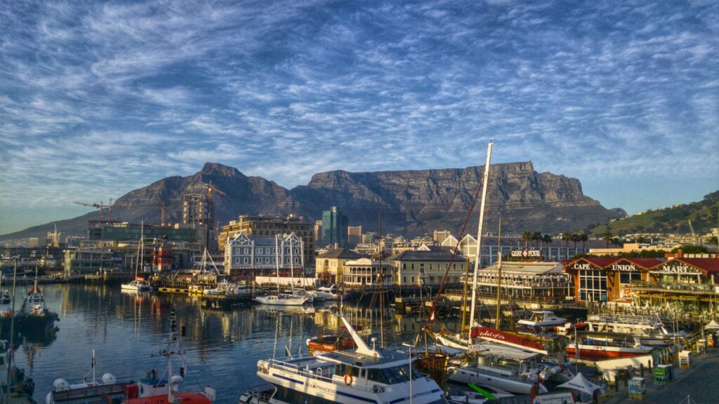 Alt text: Malerischer Hafen in Kapstadt mit Bergen, Yachten und Wolken am Himmel, perfekt für Afrika Reisen.