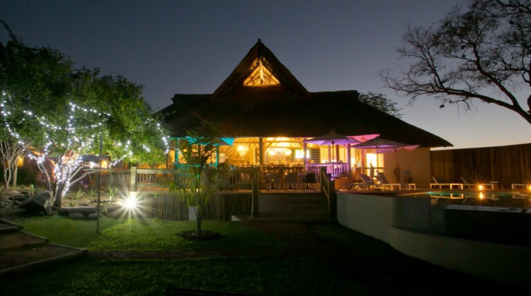Strandhotel in Afrika mit Pool und Lagerfeuer, nächtliche Urlaubsstimmung.