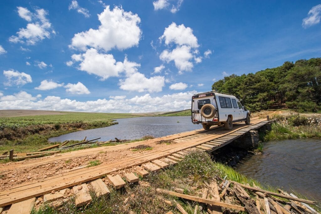 Ein Geländewagen überquert eine Brücke in der Wildnis, umgeben von Fluss und Savanne, ideal für Safari- und Natururlaub in Afrika.