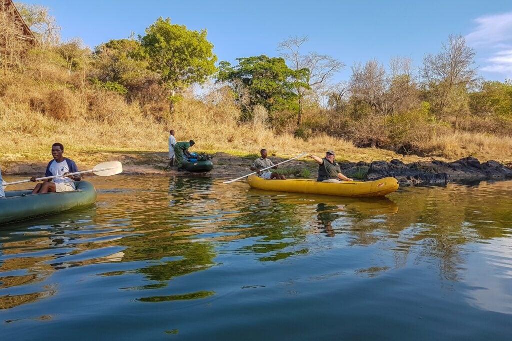 Männer erkunden den Fluss in Kanus, umgeben von afrikanischer Natur und Flusslandschaft.