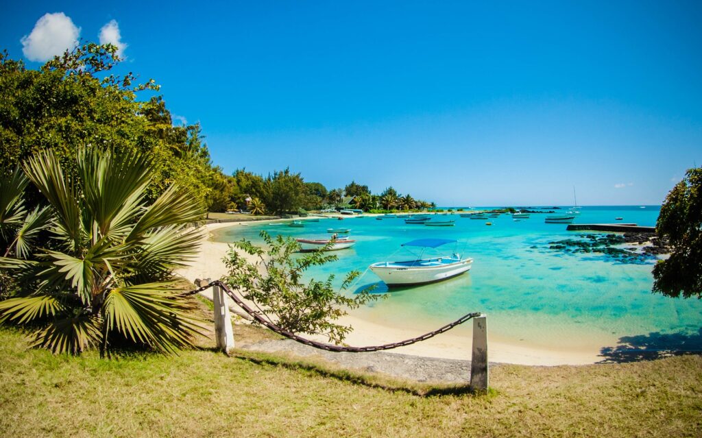 Gepflegte, tropische Küste mit weißen Booten, Palmen, Sandstrand und türkisfarbenem Wasser in Afrika.