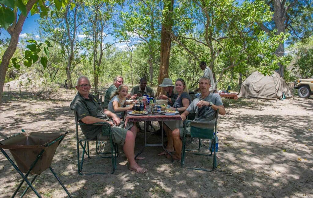 Menschen sitzen beim Buschessen in Afrika, umgeben von Bäumen.
