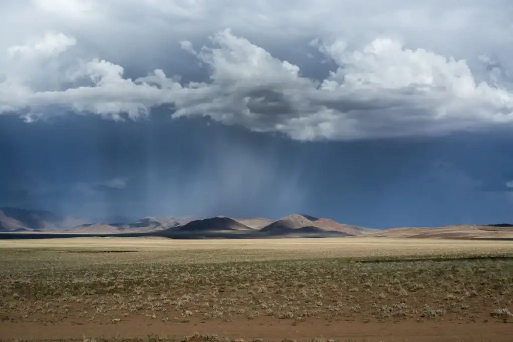 Naturreise in Afrika: Afrika-Savanne mit Wolken, Regen und Bergen im Hintergrund.