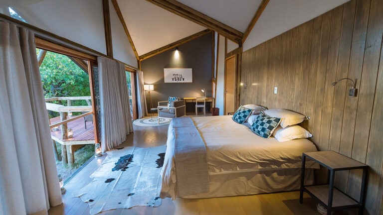 Helles Safari-Zimmer mit Holzwand und Sicht auf den Balkon in Afrika.