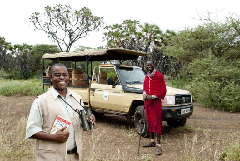 Ein Guide und ein masai stehen vor einem Safarifahrzeug bei einer Safari in Kenia