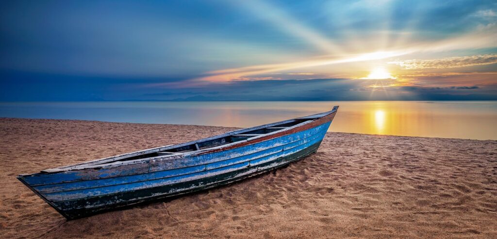 Alt Text: Verwittertes Holzboot an einem Sandstrand bei Sonnenuntergang in Afrika, ruhige Meereslandschaft.
