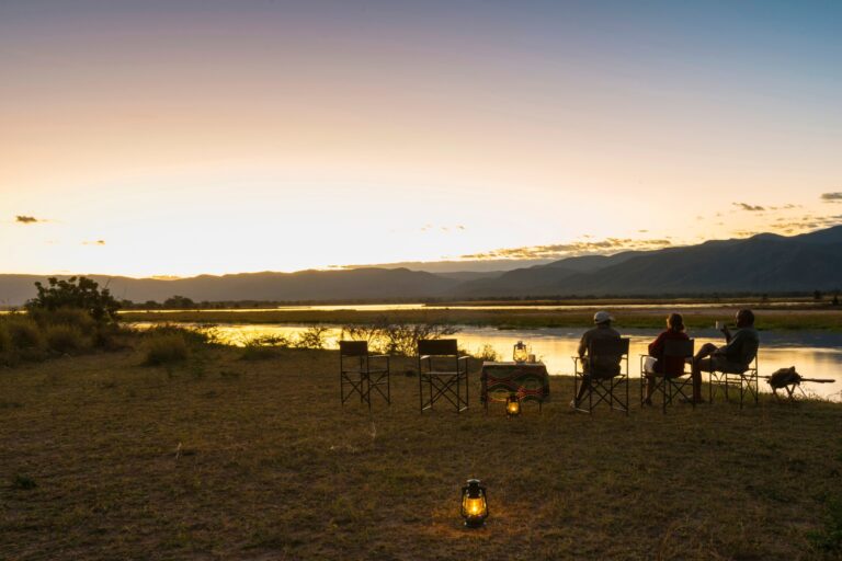 Menschen genießen Sonnenuntergang am Fluss in Afrika, Safari, Wildtiere, Naturerlebnis in Afrika.