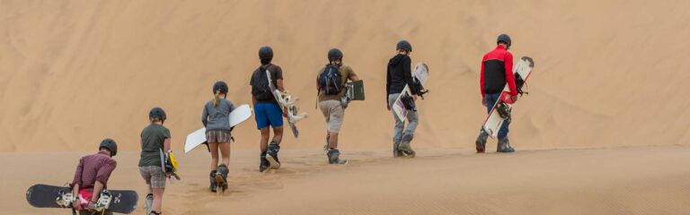 Abenteurer beim Sandboarden in der Sahara, mit Helmen in ägyptischer Wüste, spannende Afrikareise.