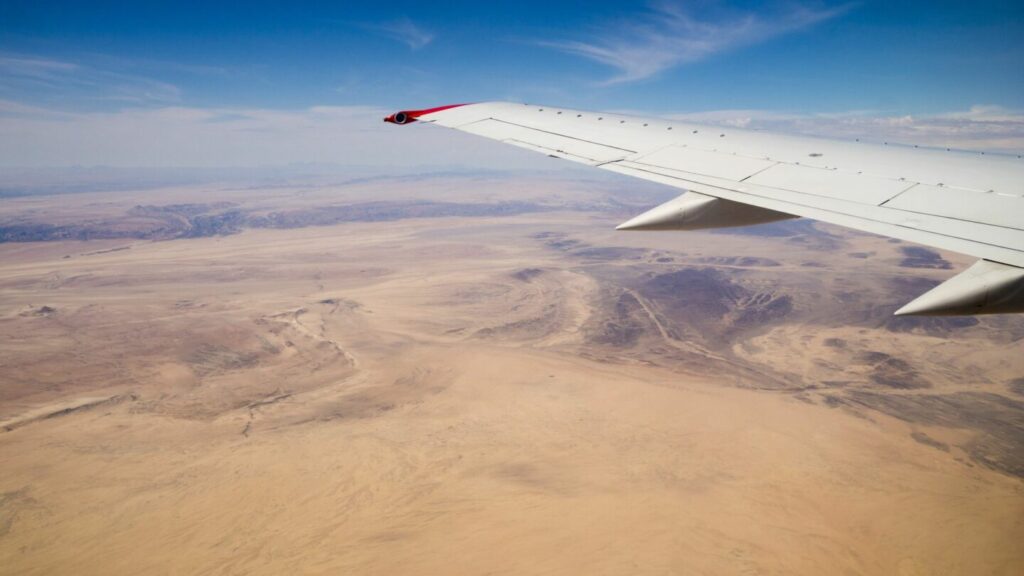 Flugzeugflügel über Wüstenlandschaft in Afrika.