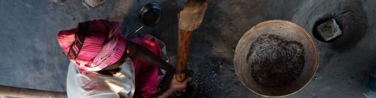 Traditionelle afrikanische Frau beim Mahlen von Getreide, authentischer Kulturreise in Afrika.