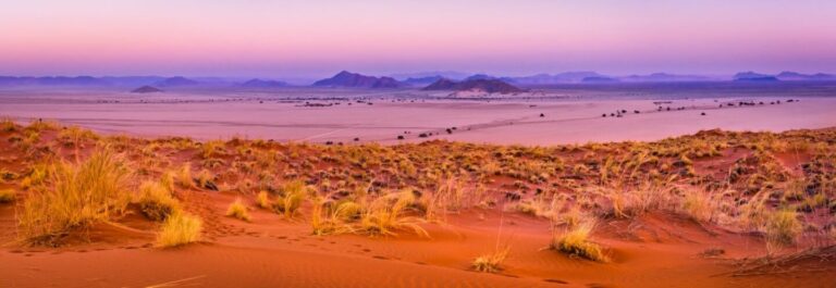 Weite Wüstenlandschaft mit Sanddünen und Gras, atemberaubender Sonnenuntergang, Wüstentour Afrika.