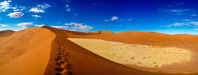 Alt Text: Sanddünen in Namibia mit Fußspuren, blauer Himmel und Wüstenlandschaft, Afrika Reiseszene.