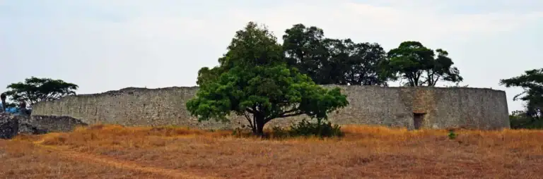 Alte afrikanische Festungsmauer in der Savanne, umgeben von Bäumen.