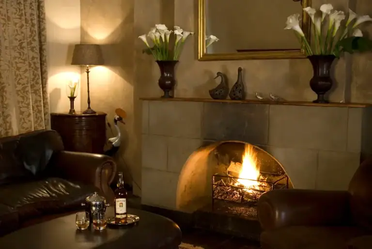 Alt Text: Wohnzimmer mit Kamin, Leder-Sofas, afrikanische Vasen und Kerzen, gemütliches Ambiente.