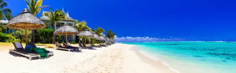 Strand mit Sonnenliegen, Bambusregenschirmen und exotischen Palmen an afrikanischer Küste.