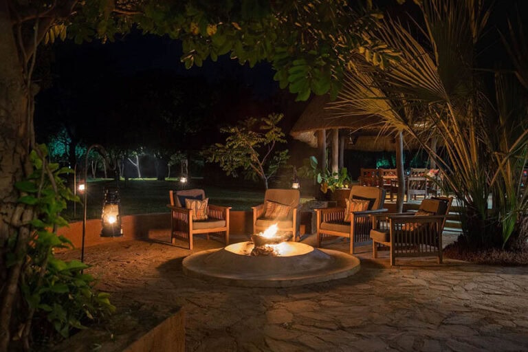 Gemütliche afrikanische Lodge mit Feuerstelle, Palmen und Garten, ideal für Afrika Safari Nächte.