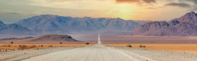 Sandstraße in der namibischen Wüste, umgeben von Bergen und klarer, weitem Himmel.