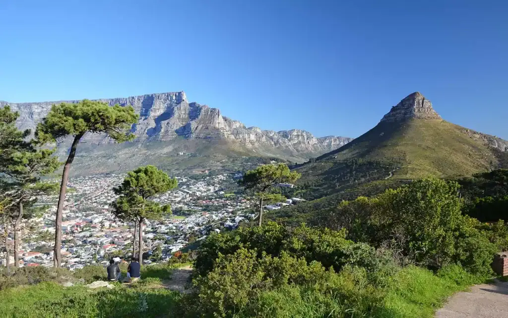 Panoramaansicht des Tafelbergs und Kapstadt mit blauer Himmel, grünen Hügeln und Stadt im Vordergrund.