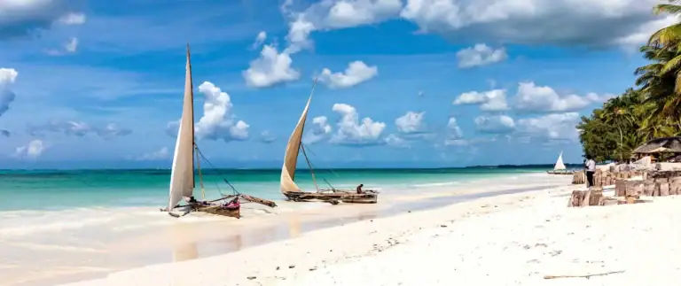 Traumhafter afrikanischer Strand mit weißen Sand und traditionellen Segelbooten, Palmen und türkisblauem Meer, ideal für Afrika Reiseerlebnisse.