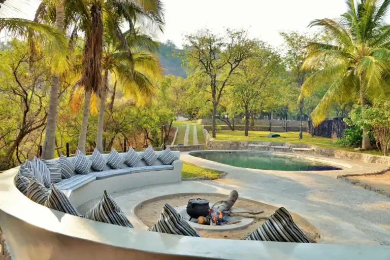 Garten mit Pool, Wasserstelle und Sitzbank im afrikanischen Safari-Urlaub, Palmen, Natur und Erholung.