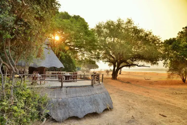 Sonnenuntergang über afrikanischer Safari Lodge mit Bäumen.