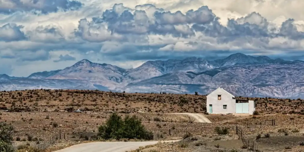 Wüstenlandschaft in Afrika, einsames weißes Haus vor Bergen, Wüsten und Wolken, Reise Afrika.