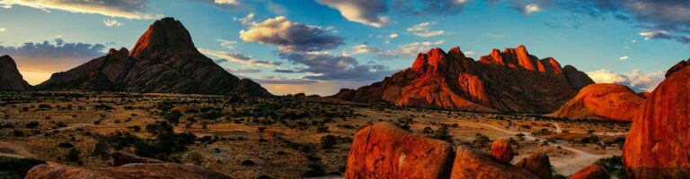 Alt: Wüstenlandschaft in Namibia mit roten Felsen bei Sonnenuntergang.
